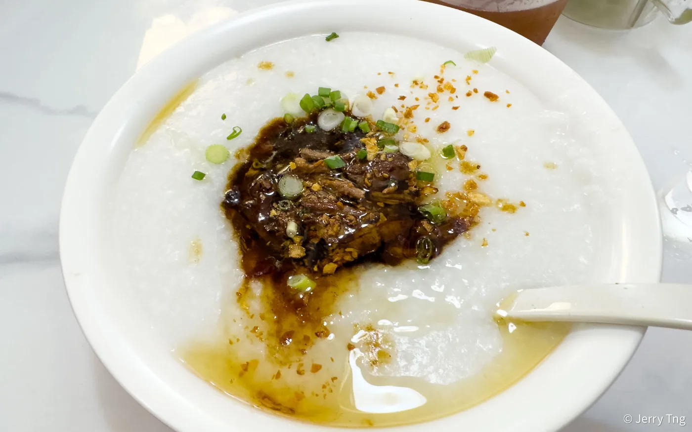 A bowl of 126 Dim Sum&rsquo;s shredded duck porridge with spring onion and condiments alongside