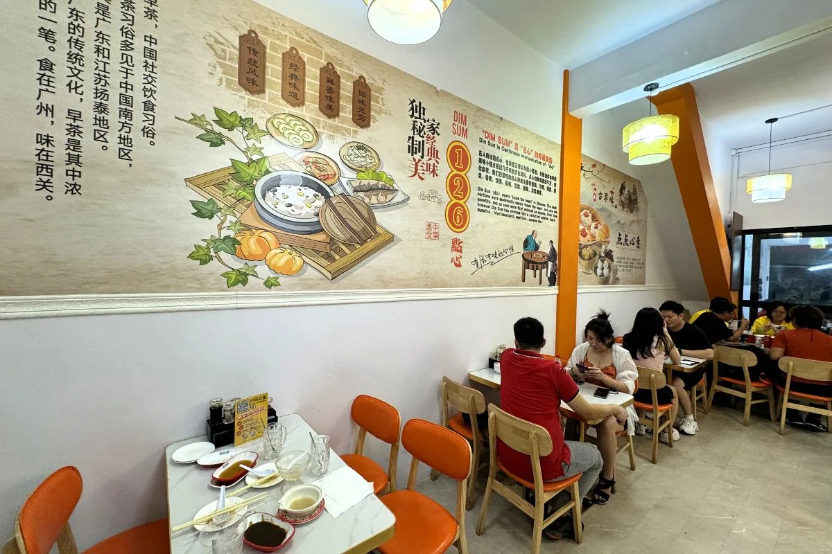 The renovated 126 Dim Sum dining room in Geylang, diners at marble tables under paper lanterns beside the painted dim sum mural
