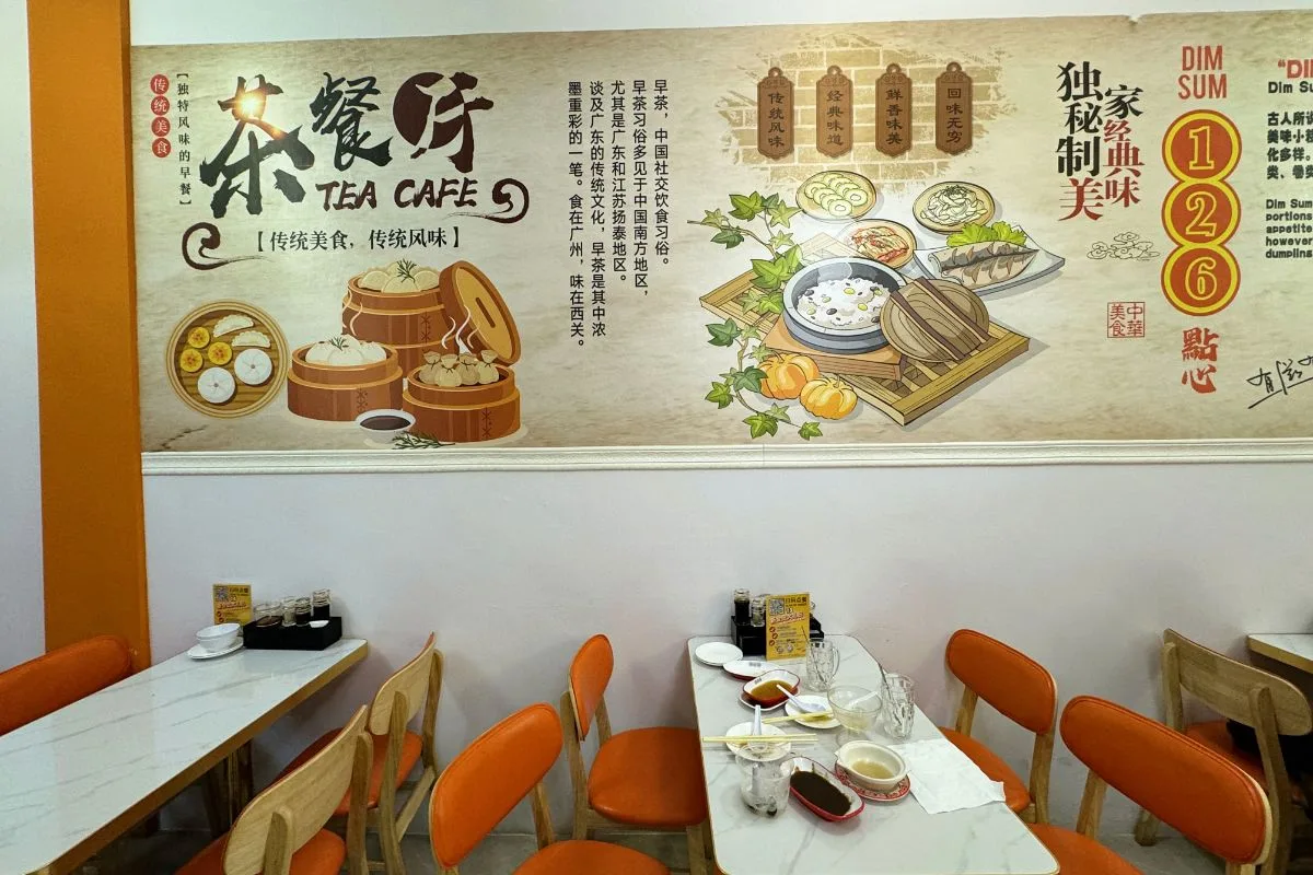 The renovated 126 Dim Sum dining room in Geylang: a painted mural of steamers and Cantonese tea-house scenes above marble tables and orange chairs