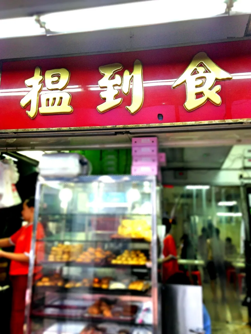 The original 揾到食 signboard in gold letters on a cherry-red board above the counter and pastry display case at 126 Sims Avenue